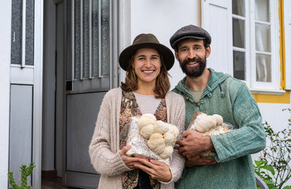 Happy man and woman holding lion's mane mushroom fruiting block grow kits outside their home. The mushroom fruiting blocks have large lion's mane mushrooms growing out of them.