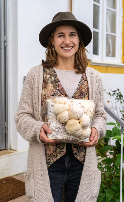 Happy woman holding lion's mane mushroom grow kit fruiting block for  easily growing mushrooms at home. The fruiting block is fully colonized and has large, premium lion's mane mushrooms growing on it.