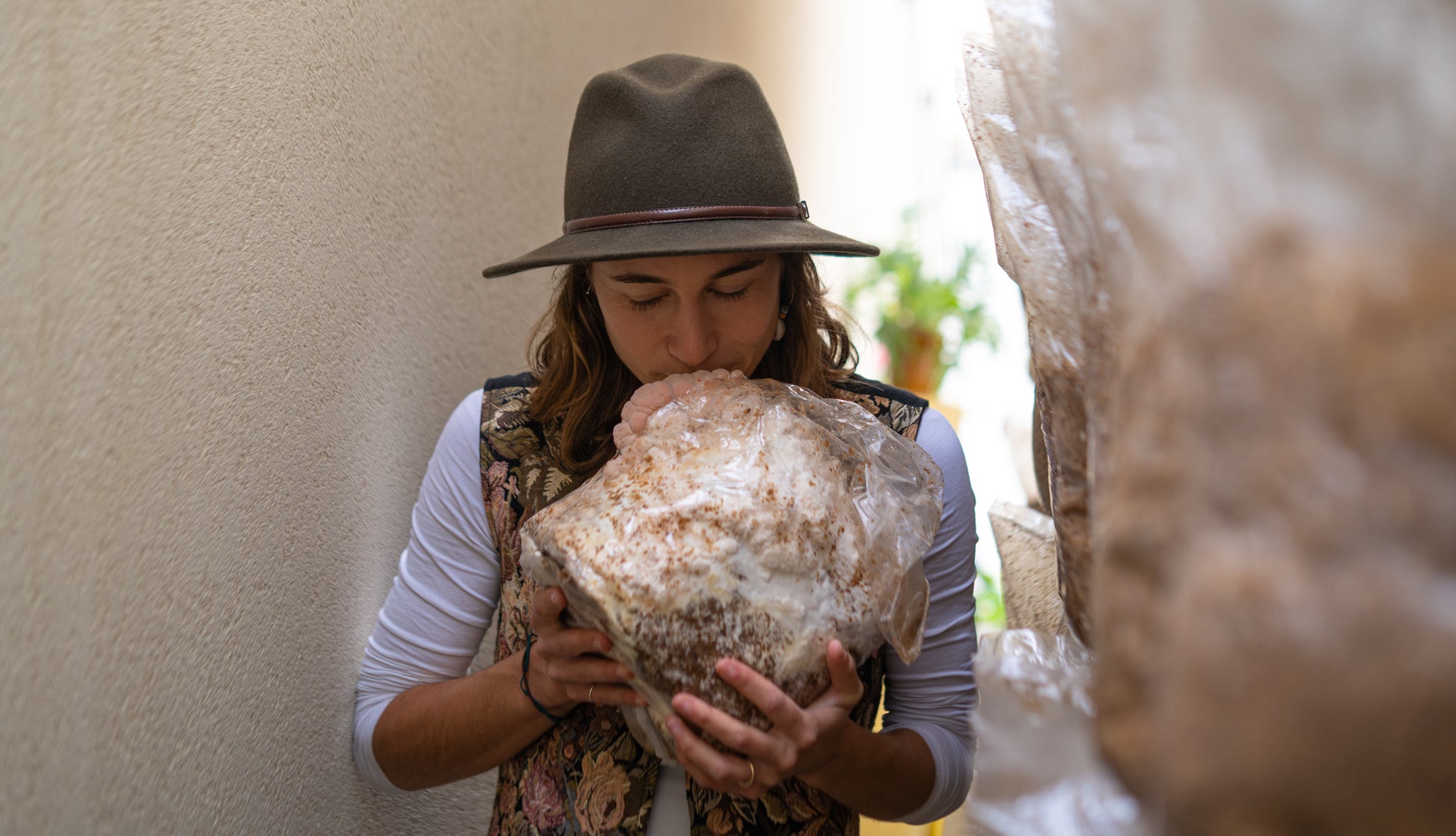 Happy woman smelling lion's mane mushroom grow kit fruiting block for  easily growing mushrooms at home. The fruiting block is fully colonized and has large, premium lion's mane mushrooms starting to grow on it.