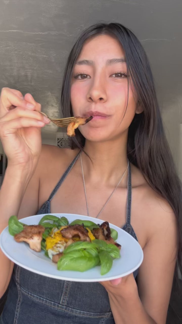 Aixa growing pink oyster mushrooms on her kitchen counter at home using a spray and grow kit from Mushroom Grow Kit Co. Video shows Aixa opening the pink oyster mushroom grow kit, cutting open the bag, spraying it with water. She then harvests the fresh mushrooms and cooks a vegan bacon recipe with them. 
